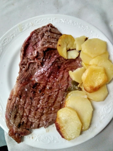 Filete a la parrilla con patatas en rodajas sobre un plato blanco.