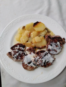 Plato con patatas en salsa y carne frita cubierta con crema blanca sobre un mantel blanco.