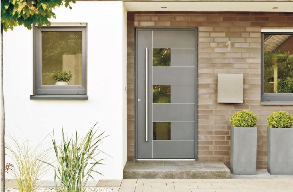 Moderne graue Haustür mit drei Glasquadraten, flankiert von Fenstern und Pflanzgefäßen.