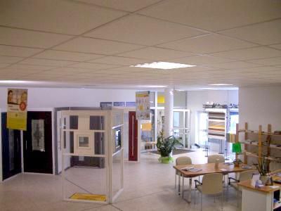 Innenansicht eines Ausstellungsraums mit Türen und Fenstern. Weiße Wände, ein Tisch und Displays schaffen eine professionelle Atmosphäre.