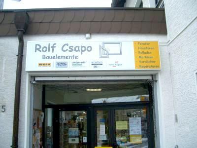 Schild für Rolf Csapo Bauelemente, ein Bauelementegeschäft. Schaufenster mit Schild und Rolltor.