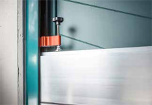 Orangefarbene Klammer befestigt weißes Material an einem blaugrünen Rahmen.