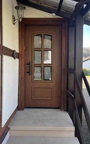 Braune Tür mit Glasscheiben in einem Holzrahmen auf einer Veranda. Weiße Wand auf der linken Seite.