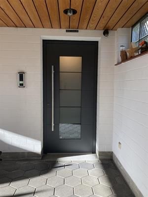 Schwarze Haustür mit Glaseinsätzen und langem Griff an einer weiß getäfelten Wand unter einer Holzdecke.