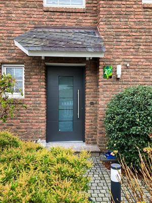 Eine dunkelgraue Haustür mit Glaseinsätzen, Backsteingebäude, Markise und Landschaftsgestaltung.