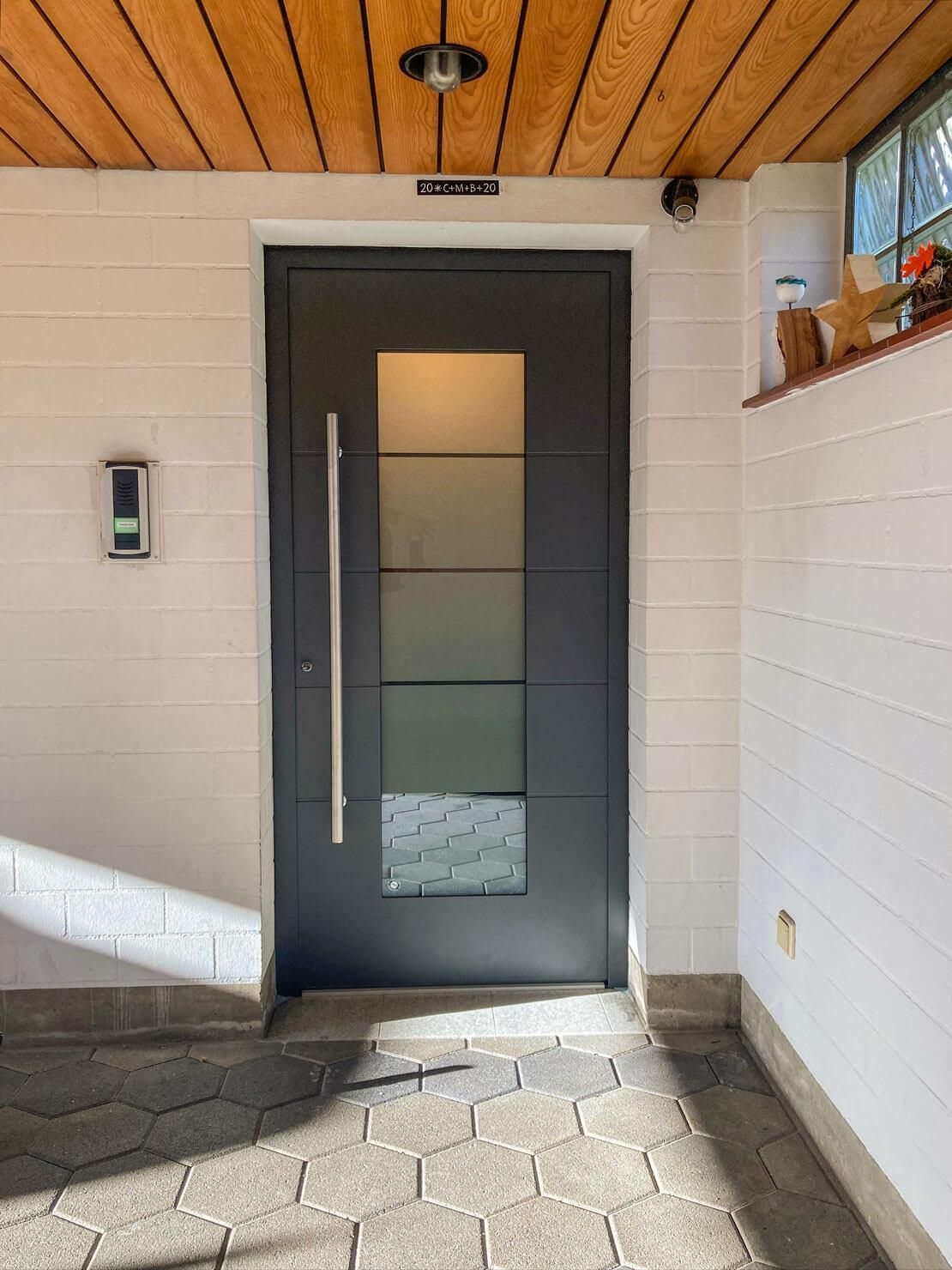 Dunkelgraue Haustür mit Glaseinsätzen, Edelstahlgriff, in einem Eingangsbereich mit weißen Wänden.