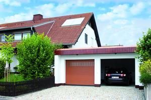 Braunes Garagentor neben einer offenen Garage mit einem Auto darin; im Hintergrund ein Haus mit rotem Ziegeldach.