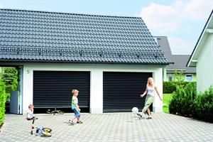 Familie spielt Fußball vor einer Doppelgarage mit geschlossenen schwarzen Türen und einem grauen Ziegeldach.