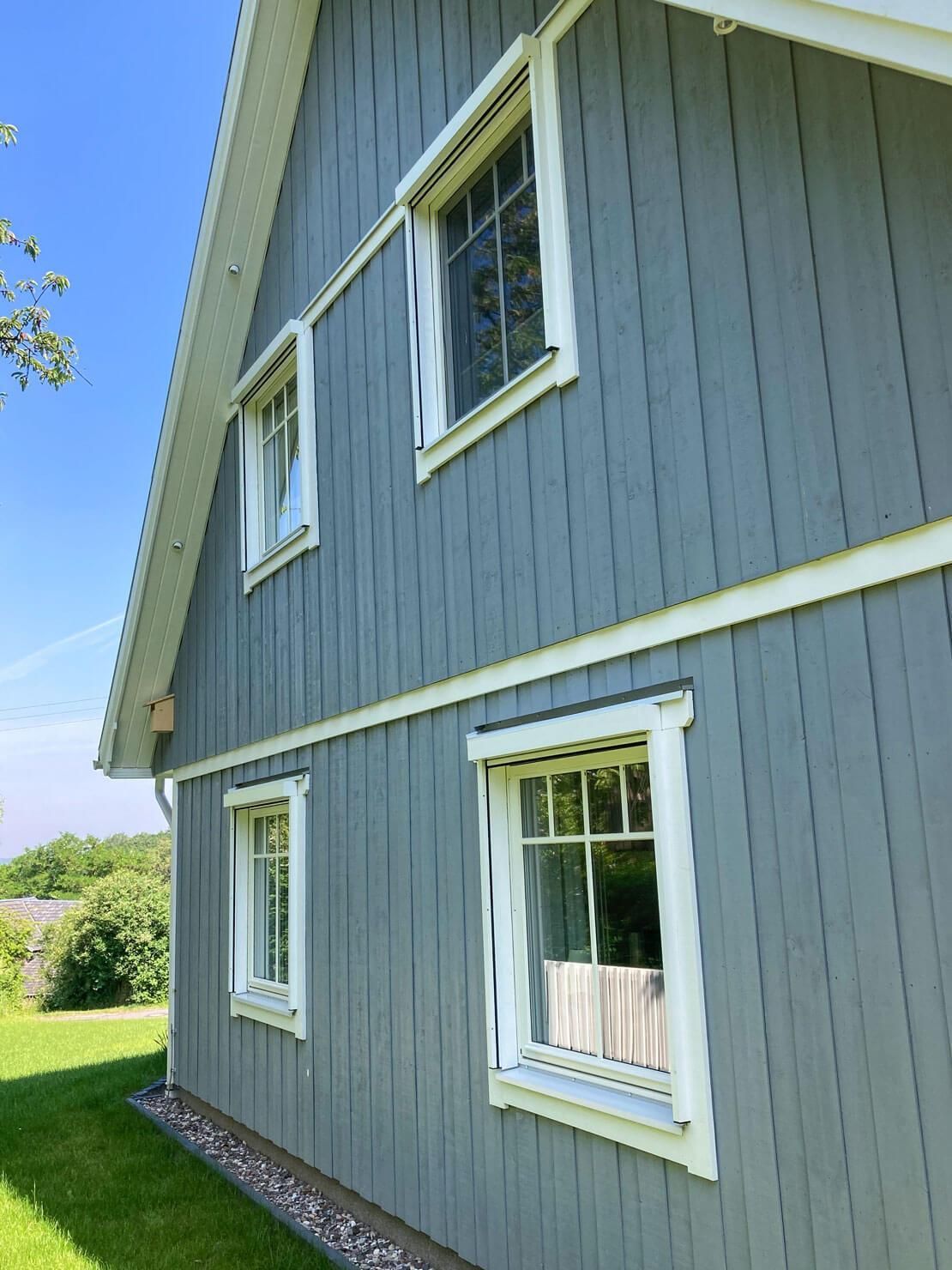 Graues Haus mit weißen Zierleisten und Fenstern an einem sonnigen Tag.