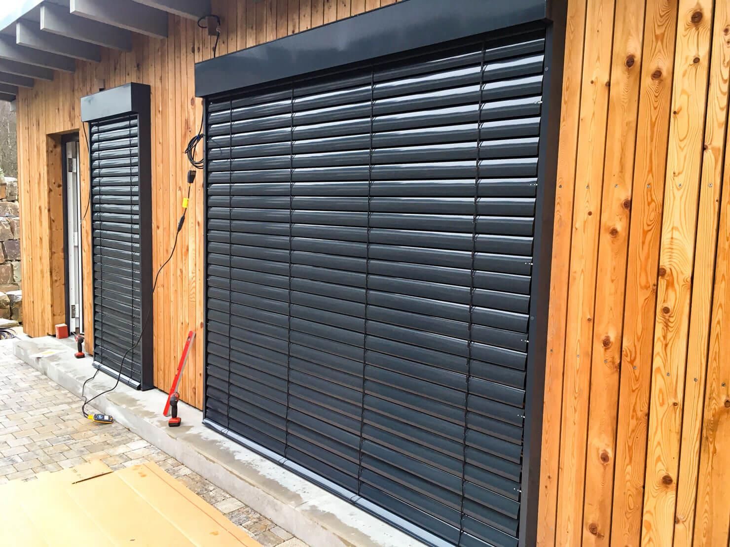 Dunkelgraue Rollläden an der Außenseite eines Holzgebäudes.