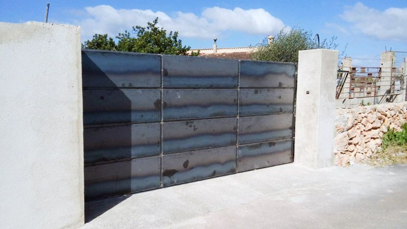 Puerta metálica entre dos pilares de hormigón en un día soleado.