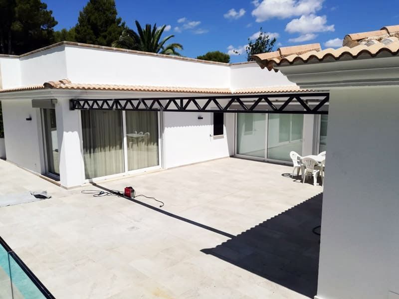Casa blanca con patio exterior, toldo negro y puertas corredizas de vidrio bajo un cielo azul.