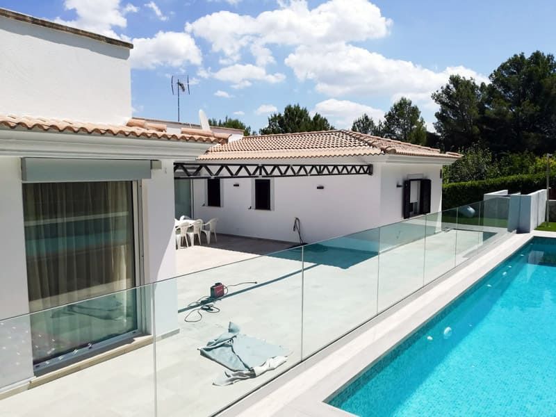 Vista de la piscina de una casa blanca con piscina y barandilla de vidrio, día soleado.