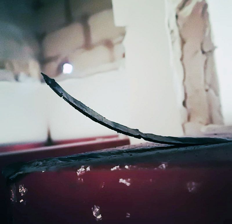 Hoja de metal curvada sobre una superficie roja, con un fondo blanco borroso.