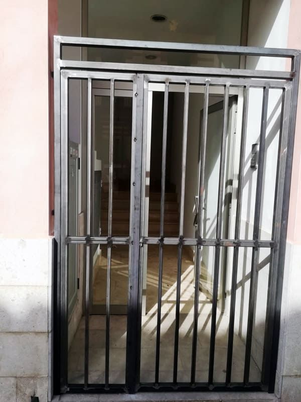 Puerta de seguridad metálica en la entrada de un edificio. Rejas negras, luz procedente del pasillo.