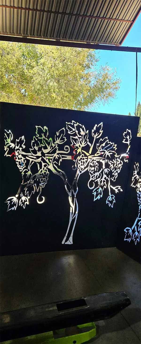 Árbol de metal negro recortado sobre un fondo negro, con un cielo verde/azul detrás.