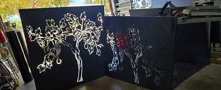 Dos lienzos negros apoyados uno sobre el otro, mostrando un diseño de árbol con líneas y colores brillantes.