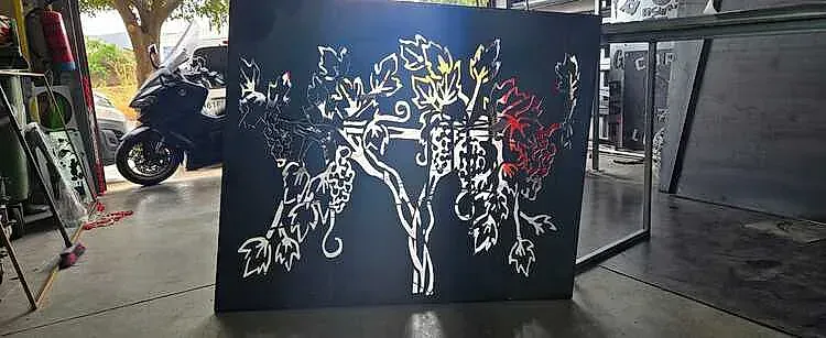 Una pieza de arte de metal negro que presenta un diseño de árbol con recortes blancos, en un garaje.