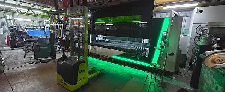 Interior de un taller con una carretilla elevadora y maquinaria. El foco principal es una gran máquina verde brillante.