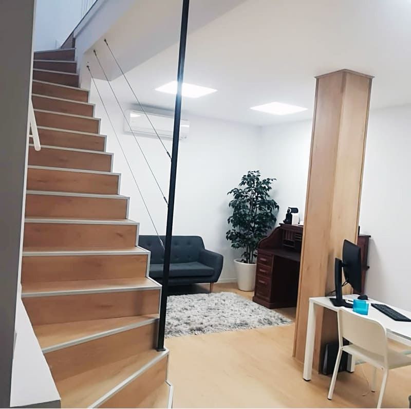 Escalera de madera que conduce a un espacio de oficina moderno con escritorio, sofá y planta en maceta.