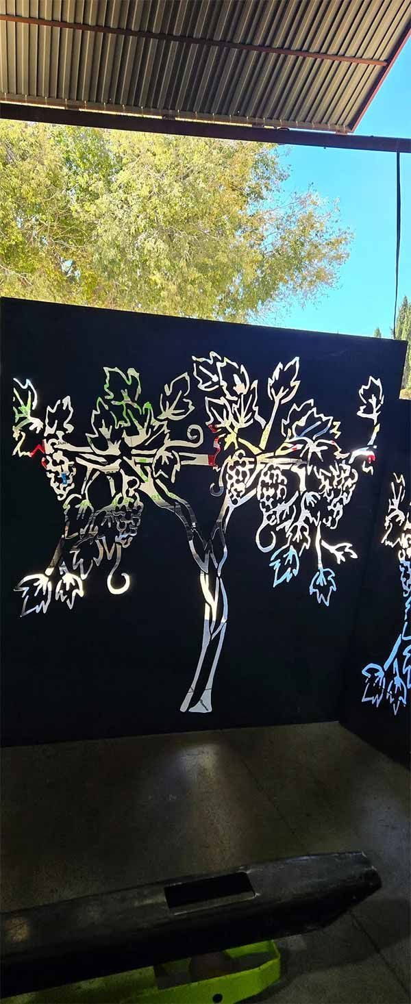 Recorte de árbol de metal negro contra un cielo azul, debajo de un techo corrugado.