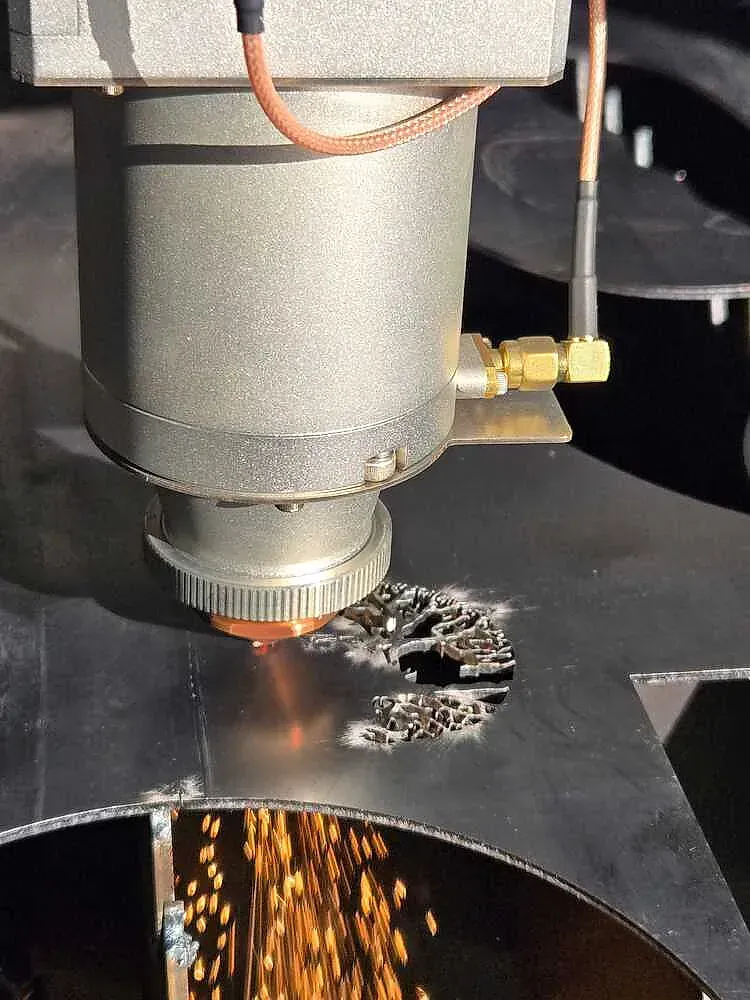 Cortadora láser cortando metal, saltan chispas y una superficie metálica con un corte circular.