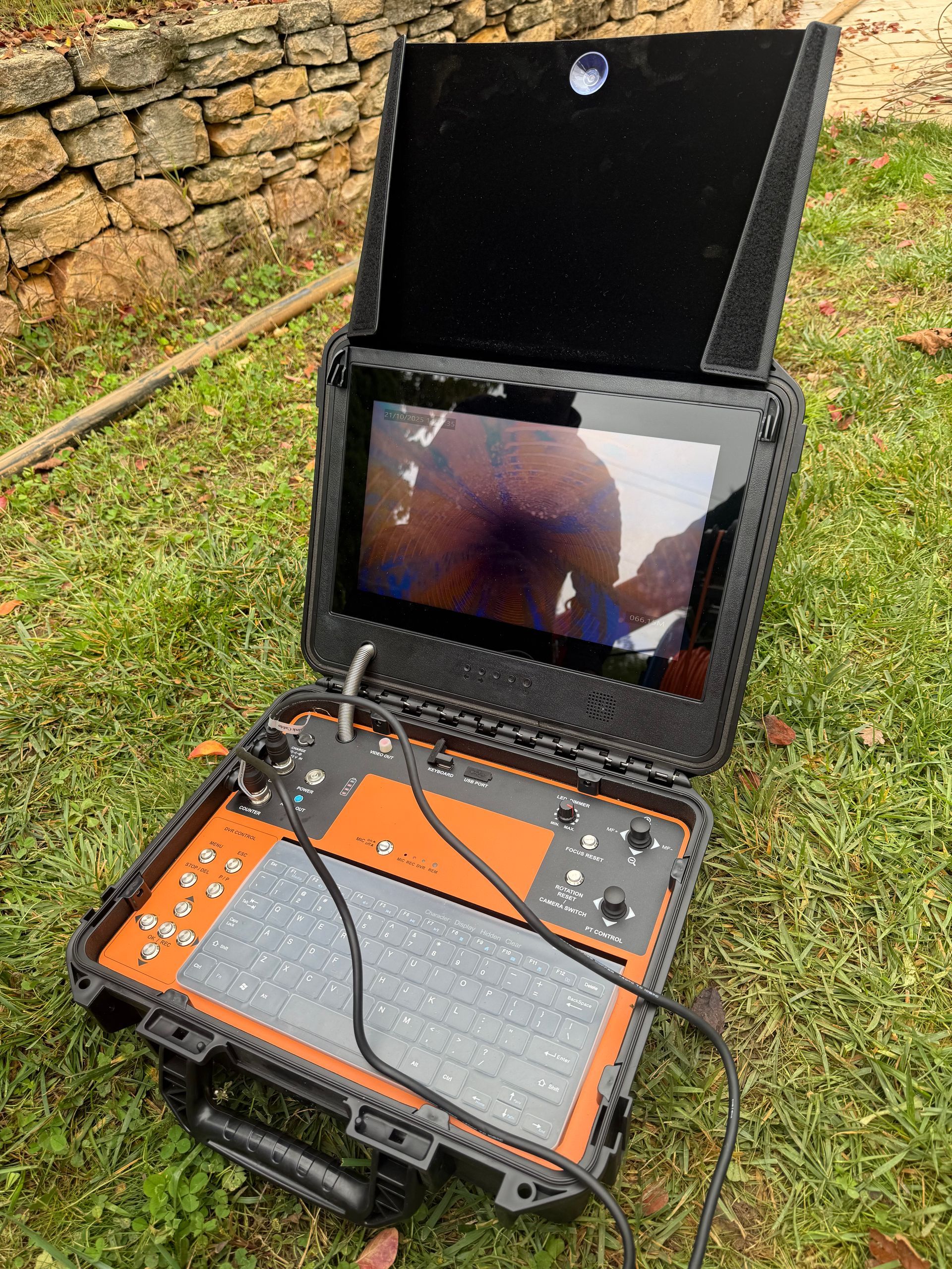 Système de caméra d'inspection portable noir et orange sur herbe verte, écran ouvert affichant une vue.