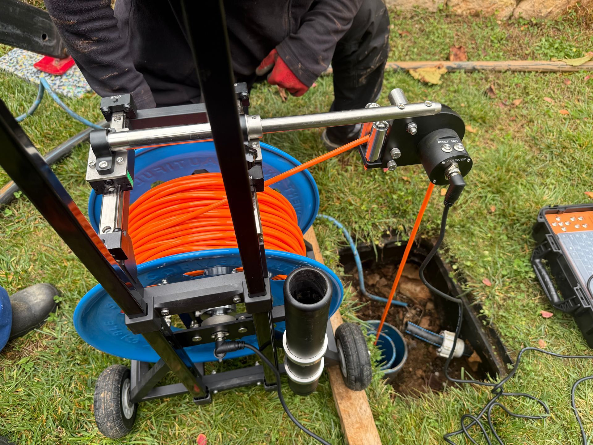 Équipement inspectant un tuyau, avec câble orange et bobine bleue, à l'extérieur dans l'herbe.