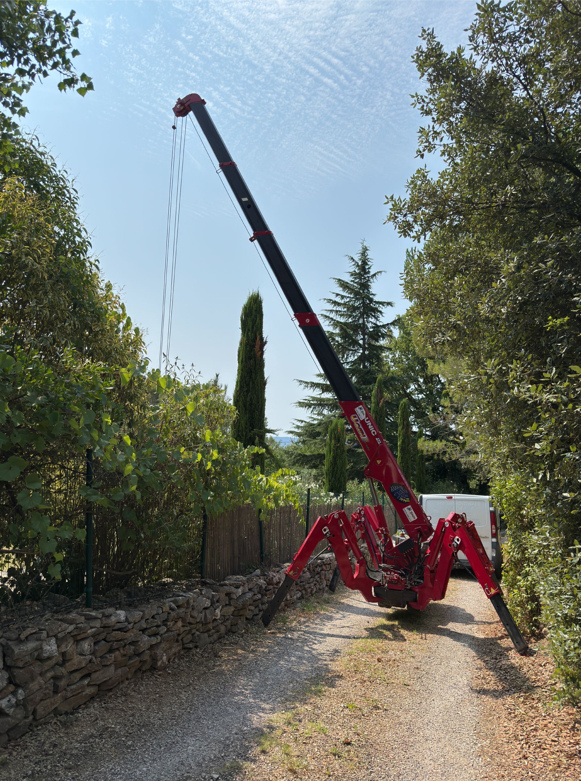 Une araignée rouge se lève sur un chemin de gravier, dépassant les arbres. Journée ensoleillée.
