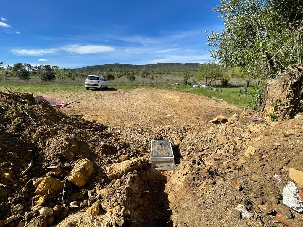Chantier de construction avec tranchée creusée et poste de conduites. Un véhicule est stationné sur une surface nivelée. Ciel bleu et paysage en arrière-plan.