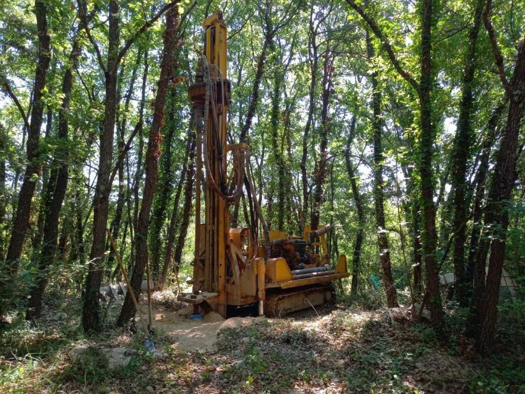 Plateforme de forage jaune dans une clairière forestière, entourée d'arbres.