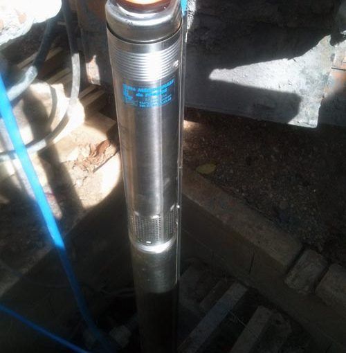 Une pompe de puits submersible en acier inoxydable est descendue dans un puits sombre.