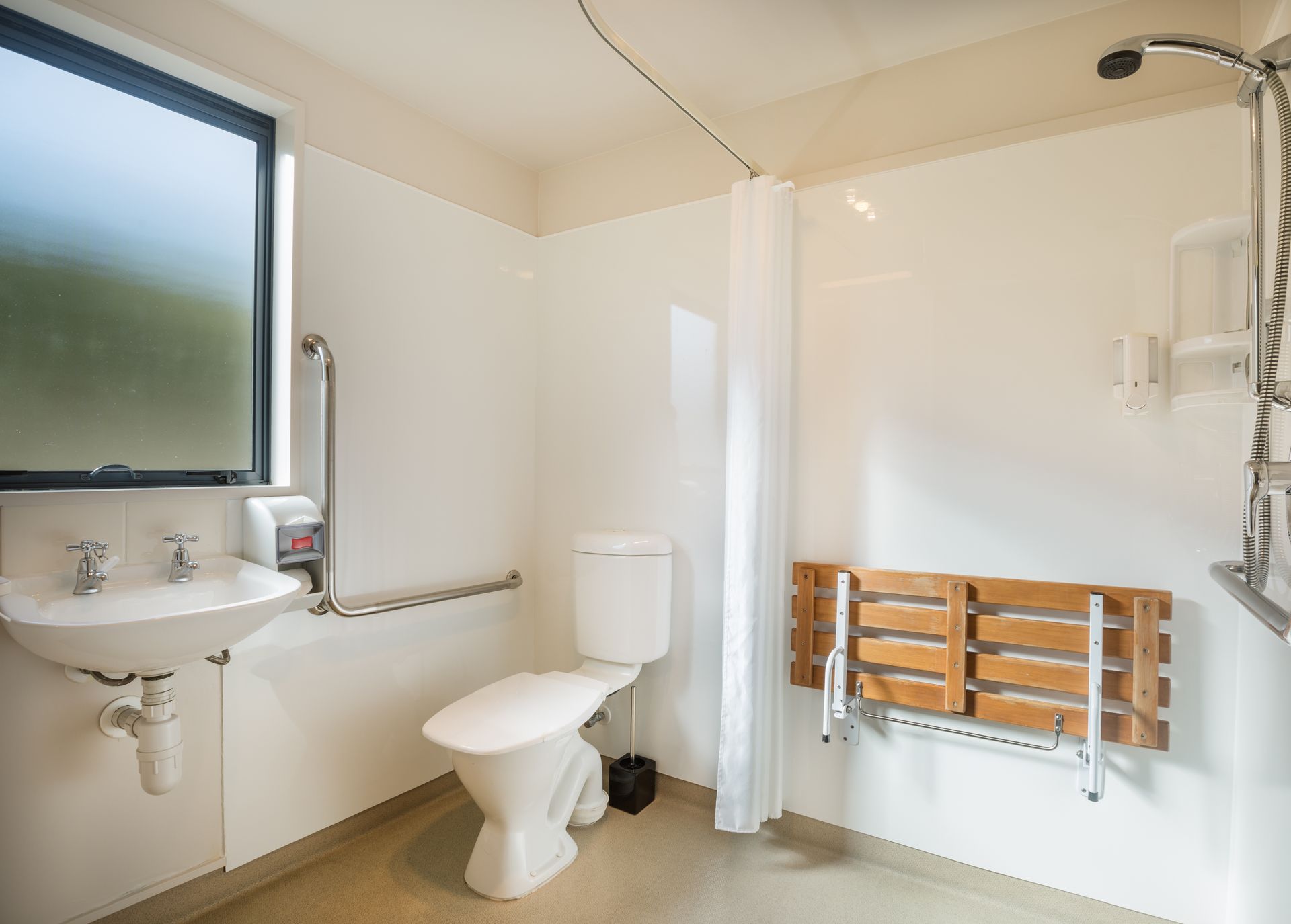 Salle de bains accessible avec toilettes, lavabo, douche avec siège rabattable et barres d'appui.