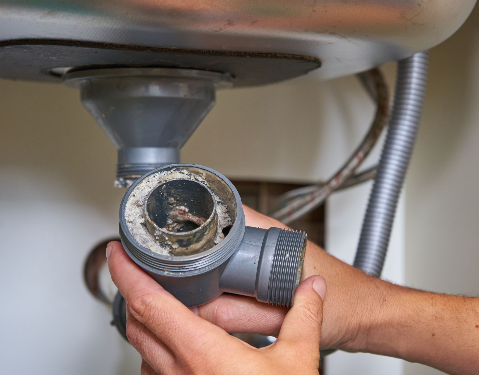Mains tenant un tuyau d'évacuation d'évier gris, le retirant pour éliminer un bouchon.