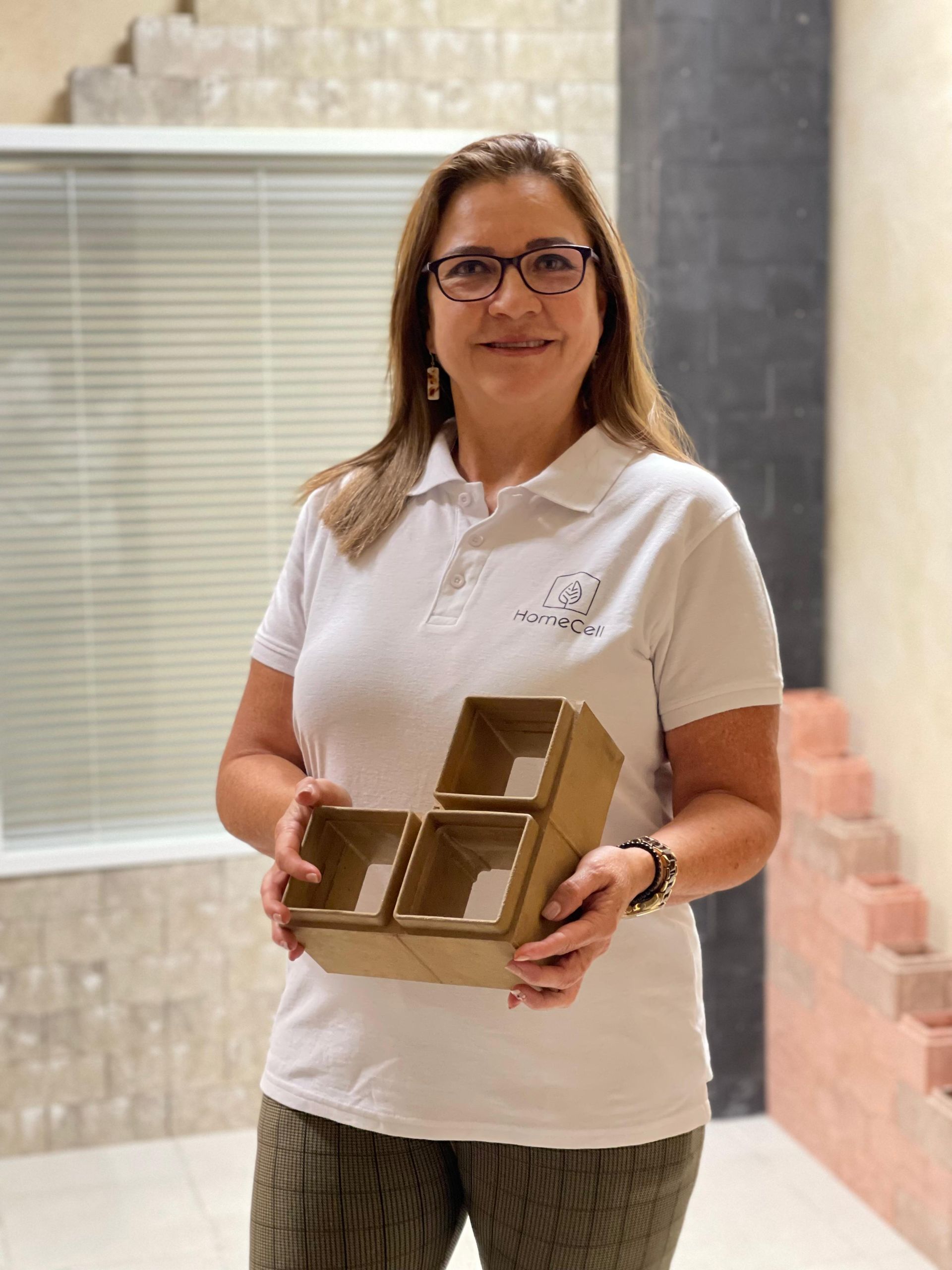 Una mujer que lleva gafas y una camisa blanca sostiene tres cajas de cartón.