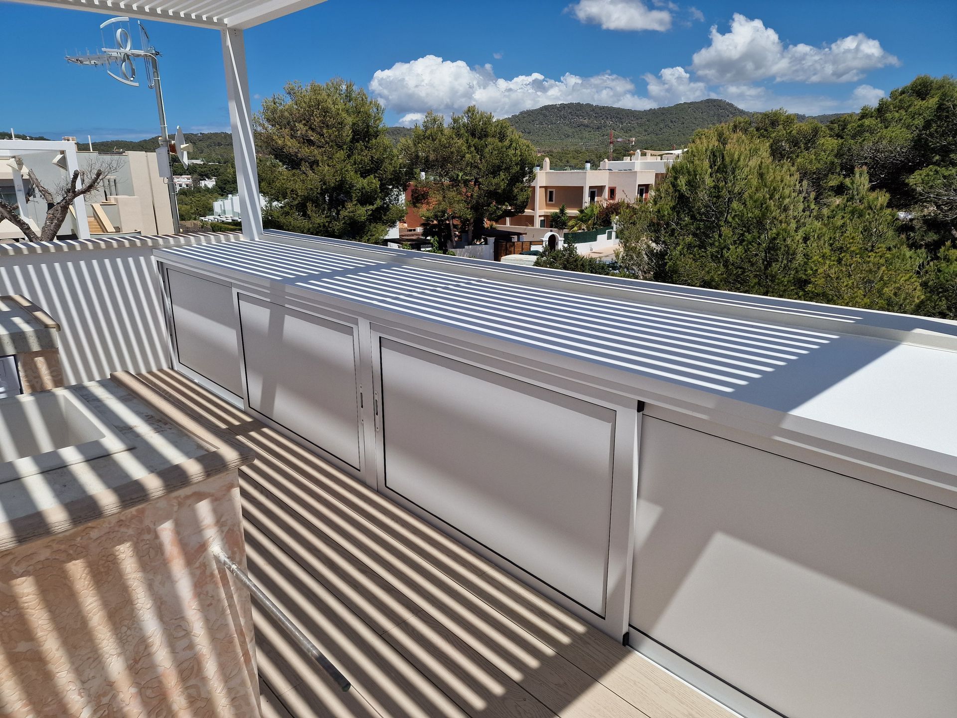 Patio blanco con pérgola, con vista a una zona residencial en un día soleado.