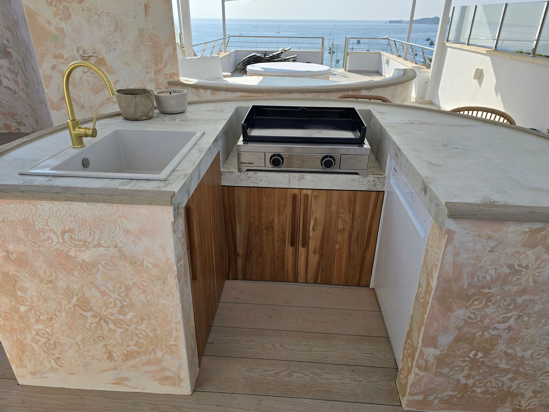 Cocina al aire libre con fregadero, parrilla y gabinetes, con vista al océano.