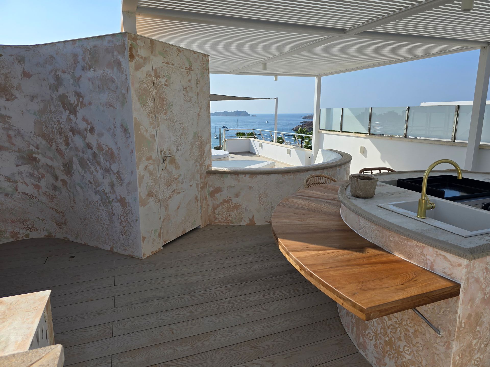 Zona de cocina exterior con superficies de madera y piedra, con vistas al mar.