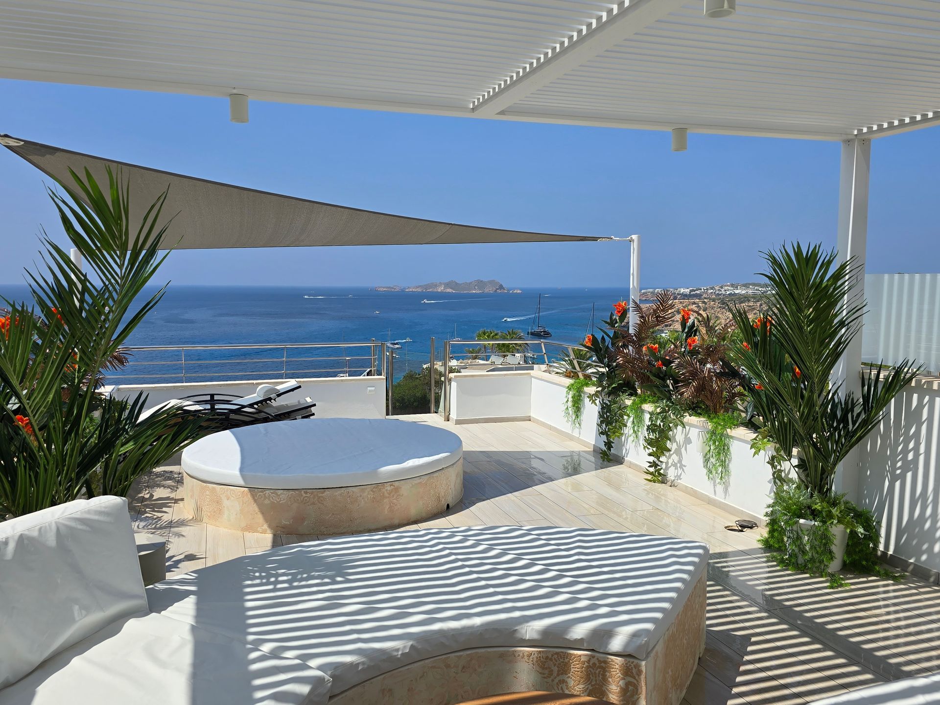 Terraza en la azotea con vistas al mar. Cuenta con un sofá cama circular, sillones, plantas y una sombrilla.