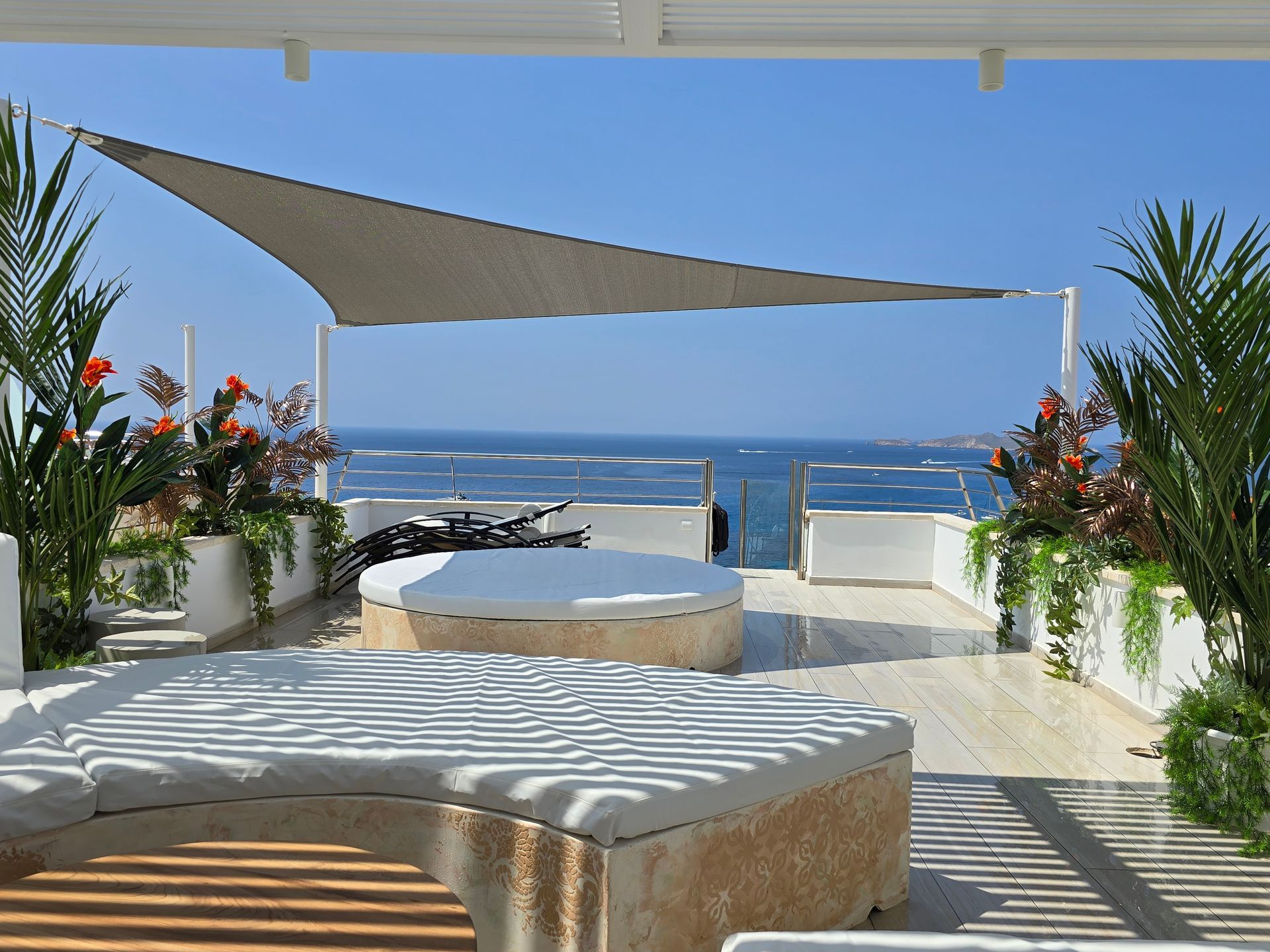 Terraza en la azotea con vista al océano, con asientos tipo lounge, velas de sombra y plantas en macetas.