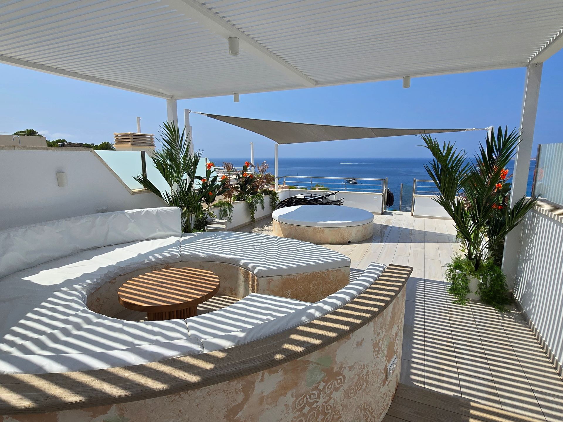 Salón en la azotea con muebles blancos, vista al mar y sombra parcial gracias a un dosel.