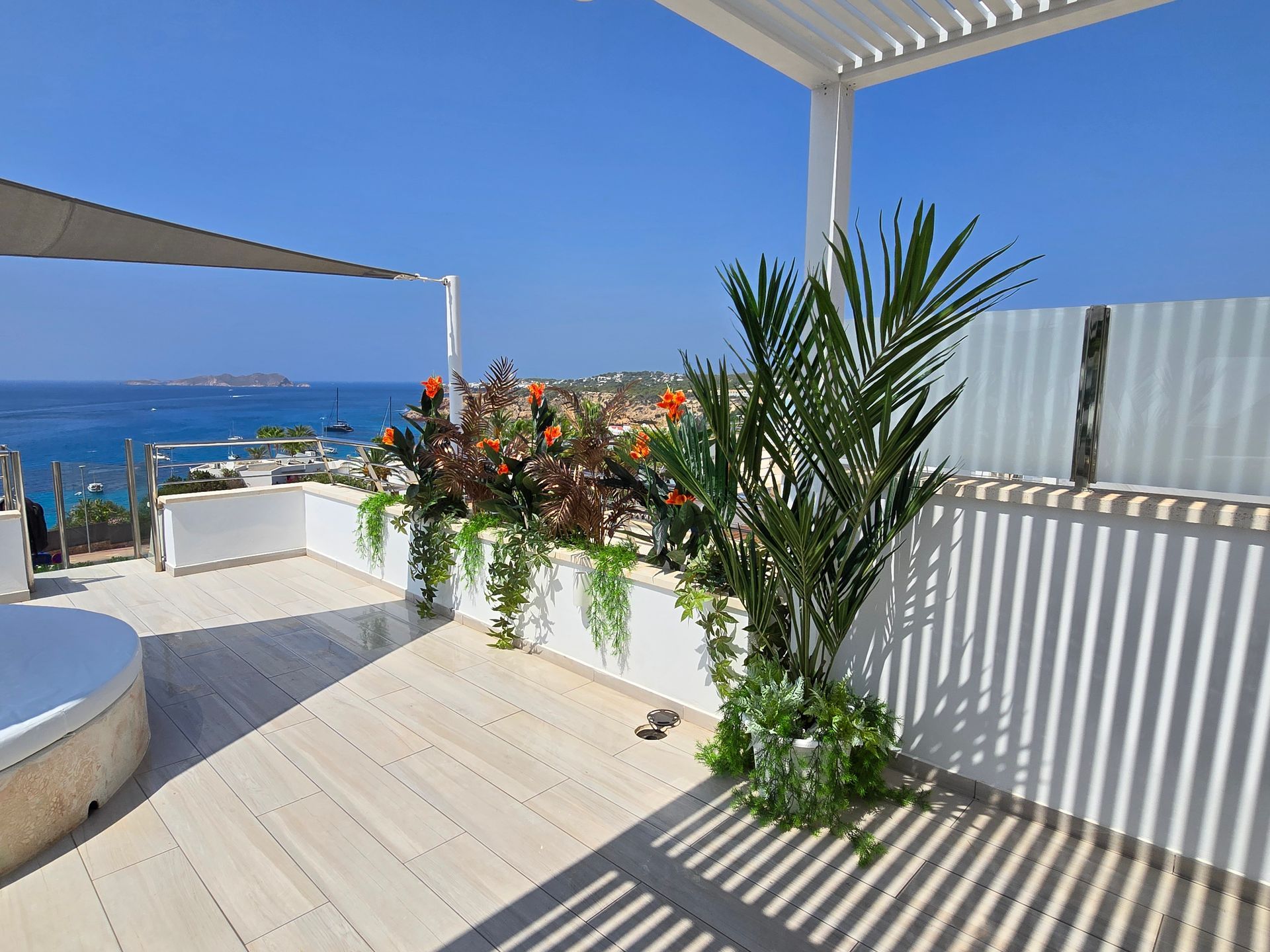 Terraza en la azotea con vistas al océano. Una pérgola blanca proyecta sombras sobre una terraza de madera clara.