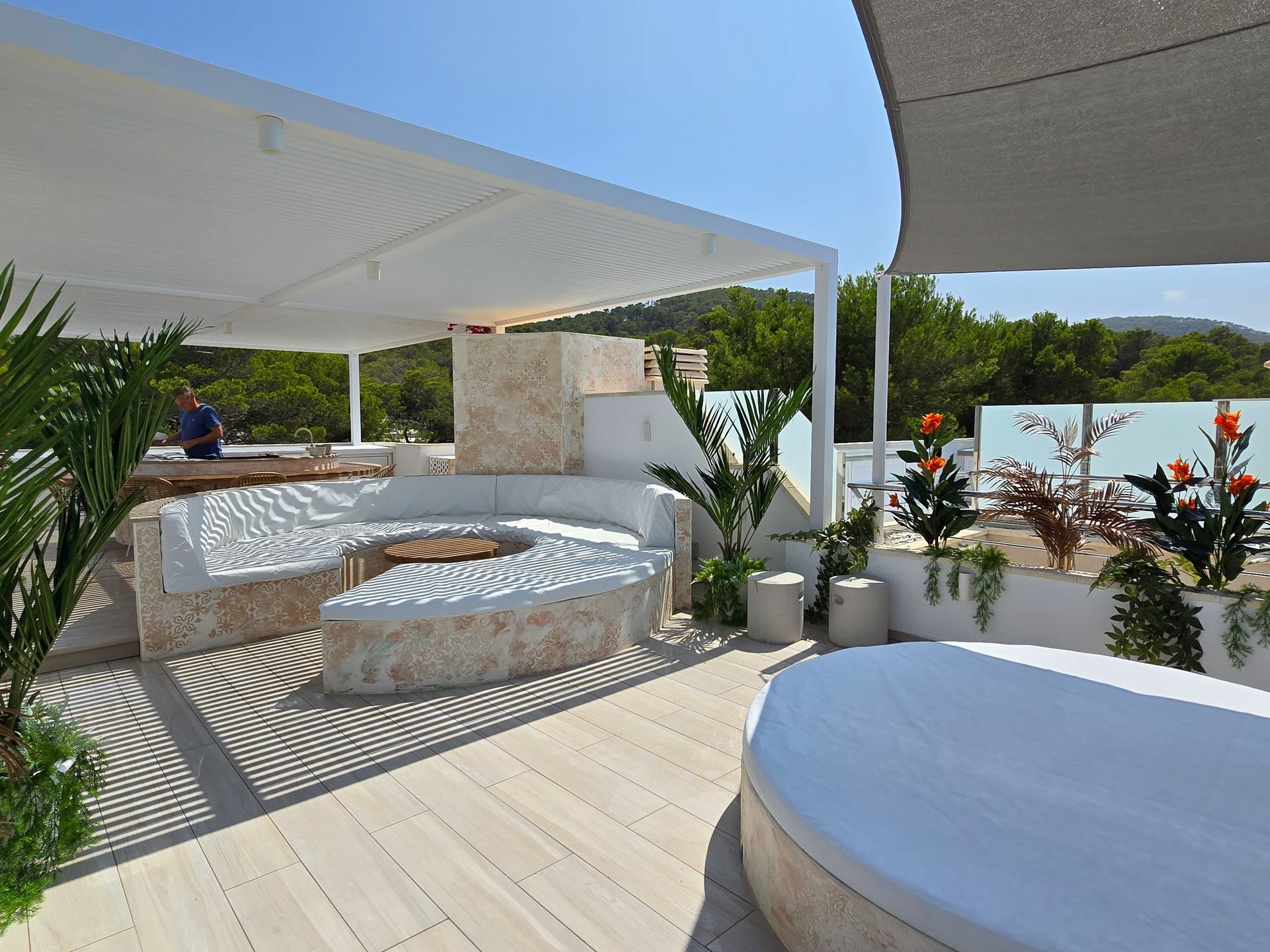 Área de salón al aire libre con fogata, asientos blancos y una pérgola cubierta.