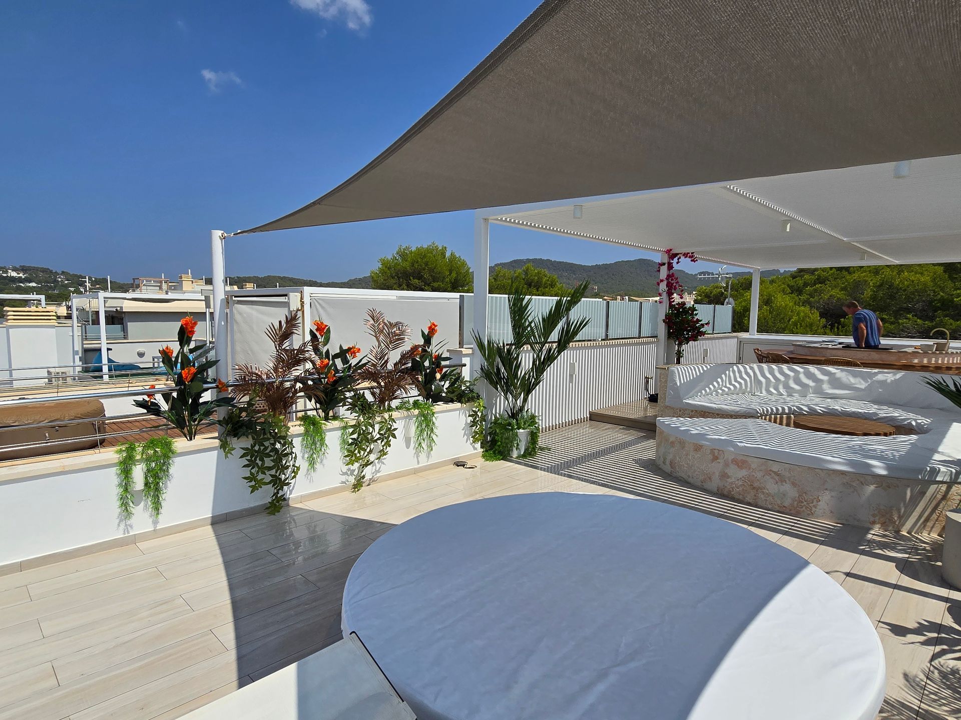 Patio en la azotea con toldo blanco, mesa de comedor y asientos empotrados. Jardineras con flores y vegetación.