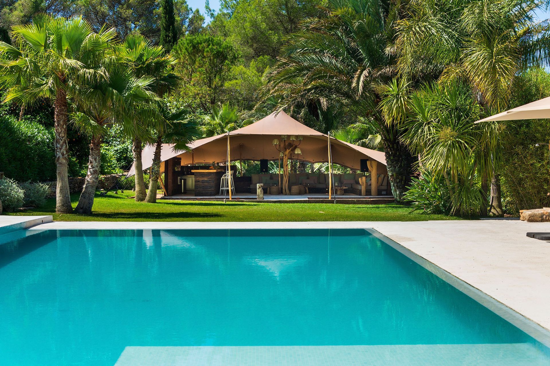 Piscina con agua turquesa, dosel sombreado y palmeras en un exuberante patio verde.