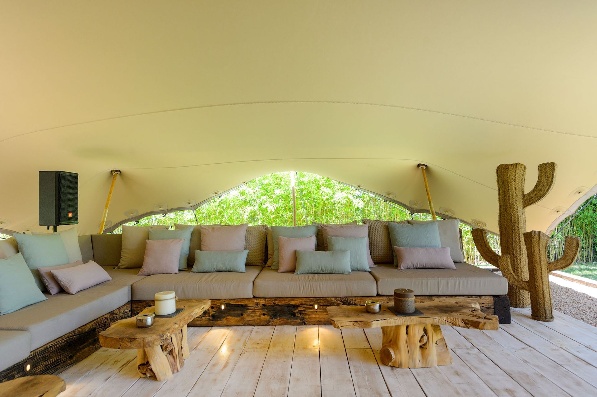 Amplio salón con lona. Sofá beige con cojines en tonos pastel, mesas de madera, decoración de cactus y suelo