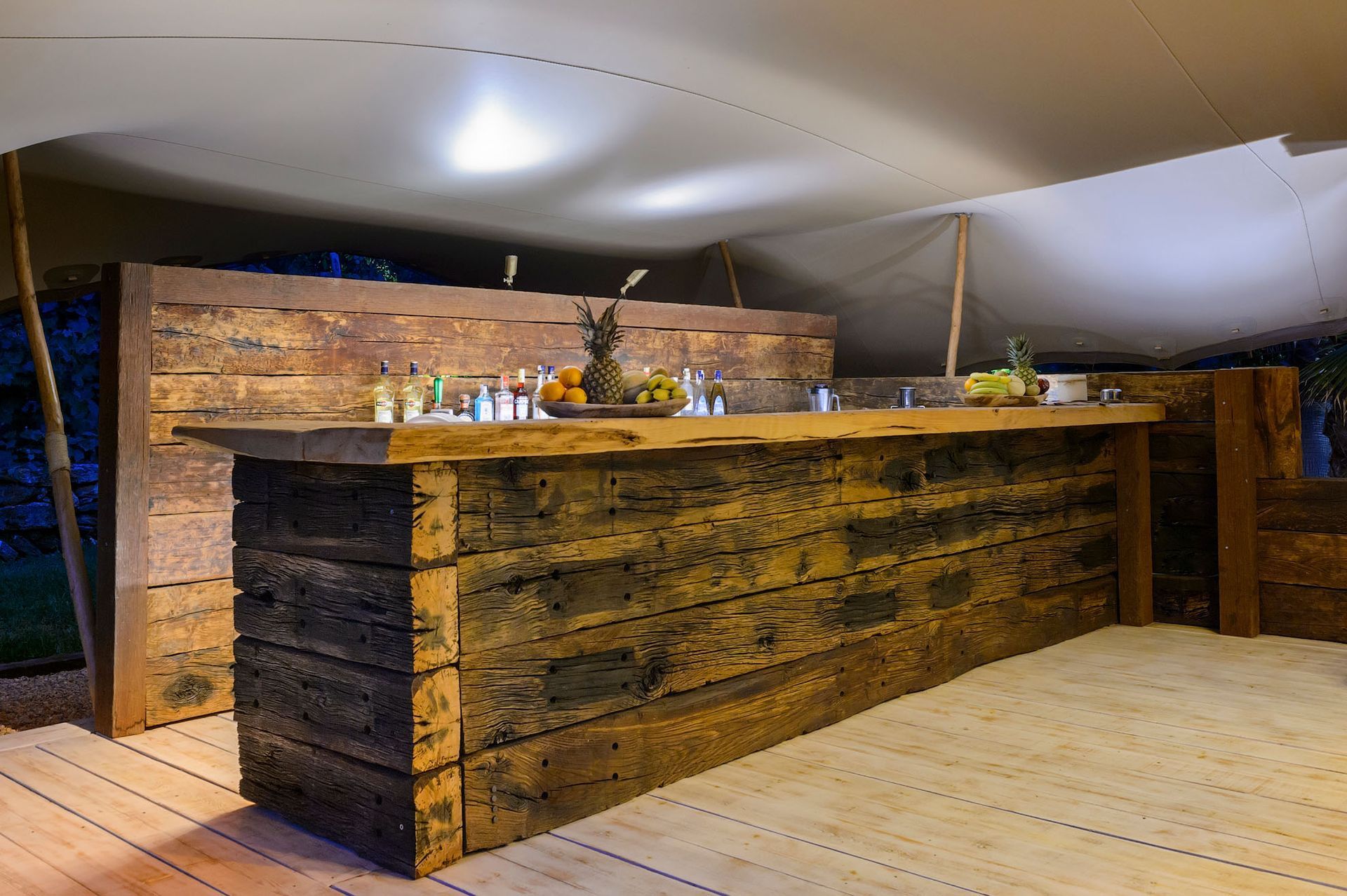 Bar dentro de una carpa con barra de madera. Bebidas, frutas y botellas se exhiben en la barra.