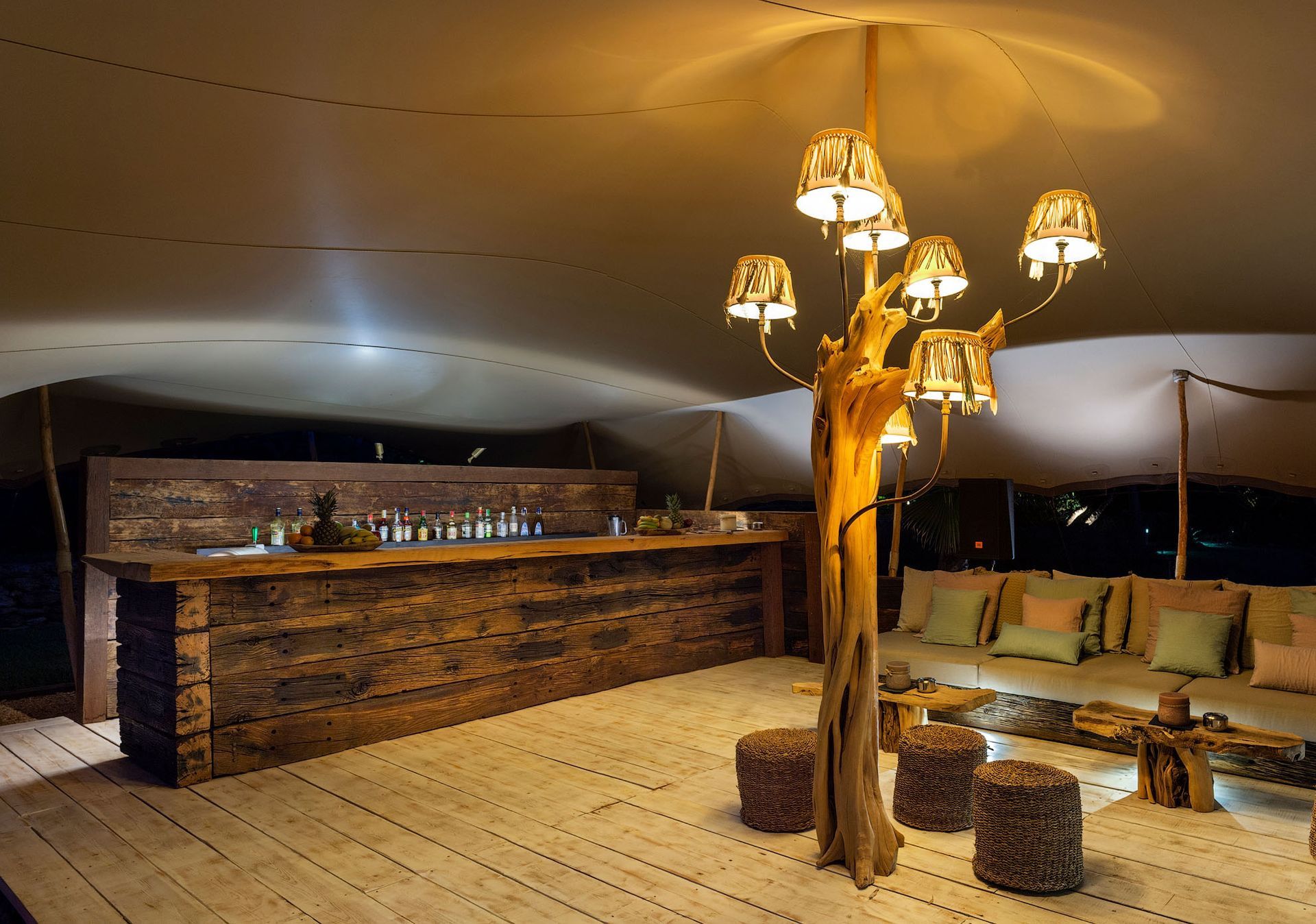 Interior de carpa de lujo con bar, zona de estar y lámpara de araña en forma de árbol.