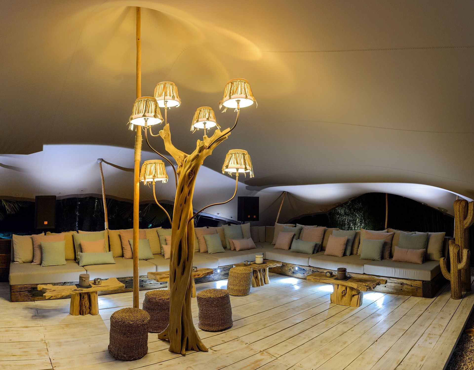 Acogedora zona de estar bajo una carpa con muebles de madera natural, iluminación suave y cojines color crema.