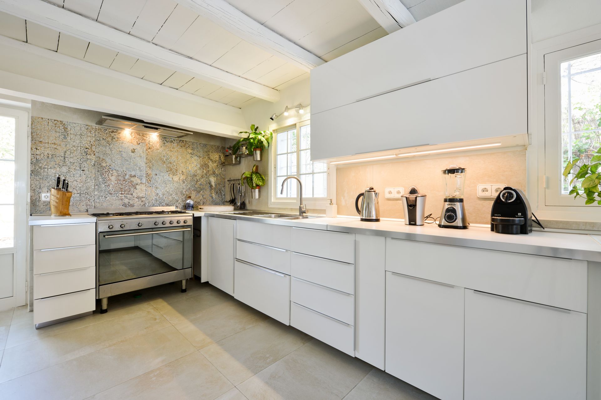 Cocina moderna blanca con electrodomésticos de acero inoxidable, salpicadero de piedra y vigas de madera.